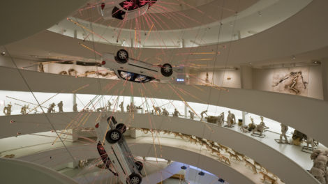 Three cars handing upside-down, each at the center of light tubes appearing as fireworks, in the rotunda of the Guggenheim Museum