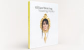 The Guggenheim publication "Gillian Wearing: Wearing Masks" against a white background. The book cover features the face of a woman with brown hair peering out of a gold mirror.