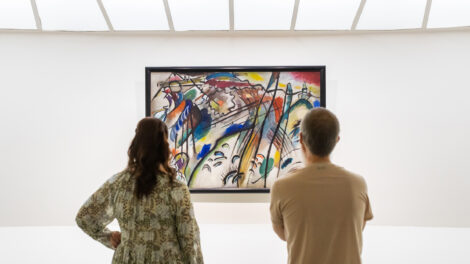 A man and a woman look at a colorful abstract painting by artist Vasily Kandinsky as it hangs on the white, curved wall of the Guggenheim Museum in New York.