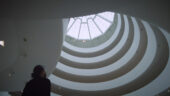 Person looking upwards towards the spiral-like architecture inside the Guggenheim museum.