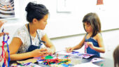 An adult and a young child at a table making art out of glue and pipe cleaners.