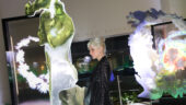 Artist Rachel Rossin, wearing a black long-sleeve dress and her platinum-blonde hair pulled up in a bun, stands amid her artworks on display at the Guggenheim Museum New York during the 2024 Young Collectors Council (YCC) Party.