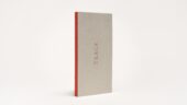 Exhibition catalogue pictured as an upright book of a neutral tone with vivid reddish-orange spine and the word trace in all caps on the cover.
